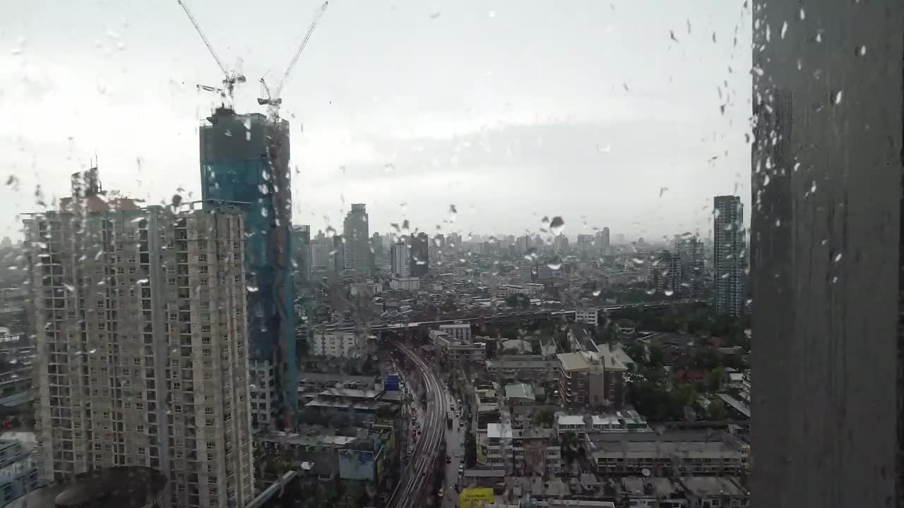 雨点落在窗户上。鸟瞰图。在泰国曼谷的雨季，起居室窗外下着雨。窗外是模糊的雨，城市建筑，道路和天空。视频素材