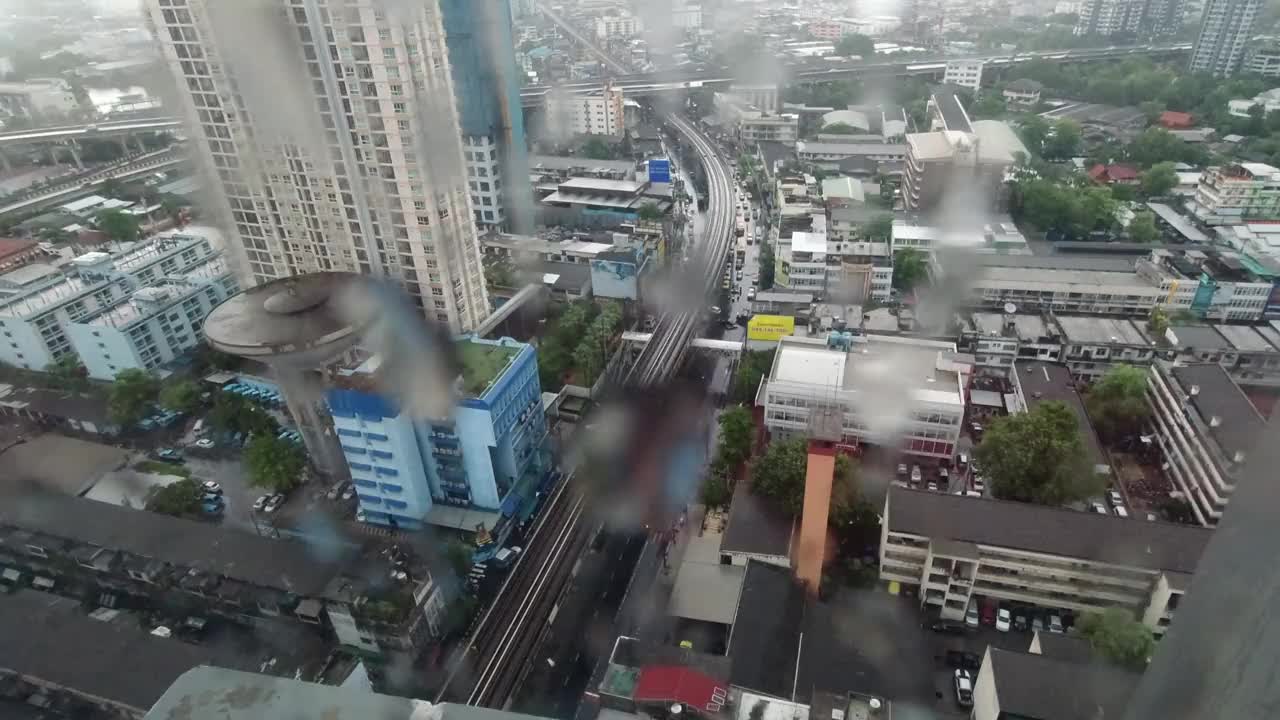 雨点落在窗户上。鸟瞰图。在泰国曼谷的雨季，起居室窗外下着雨。窗外是模糊的雨，城市建筑，道路和天空。视频素材