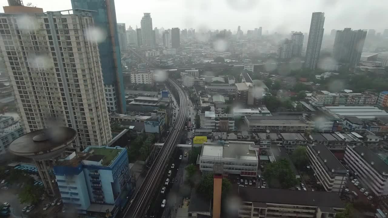 雨点落在窗户上。鸟瞰图。在泰国曼谷的雨季，起居室窗外下着雨。窗外是模糊的雨，城市建筑，道路和天空。视频素材