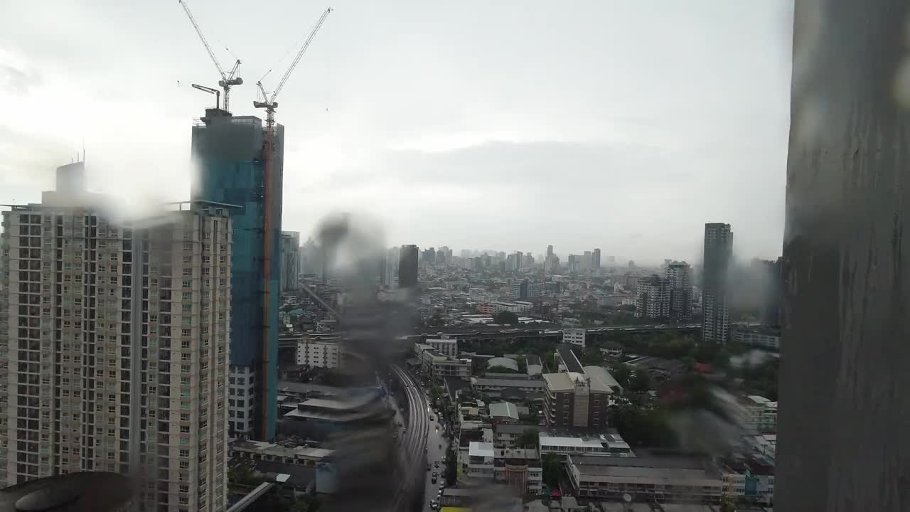 雨点落在窗户上。鸟瞰图。在泰国曼谷的雨季，起居室窗外下着雨。窗外是模糊的雨，城市建筑，道路和天空。视频素材