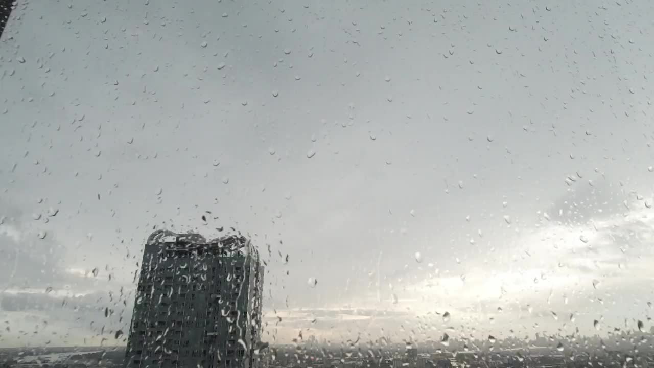 雨点落在窗户上。鸟瞰图。在泰国曼谷的雨季，起居室窗外下着雨。窗外是模糊的雨，城市建筑，道路和天空。视频素材