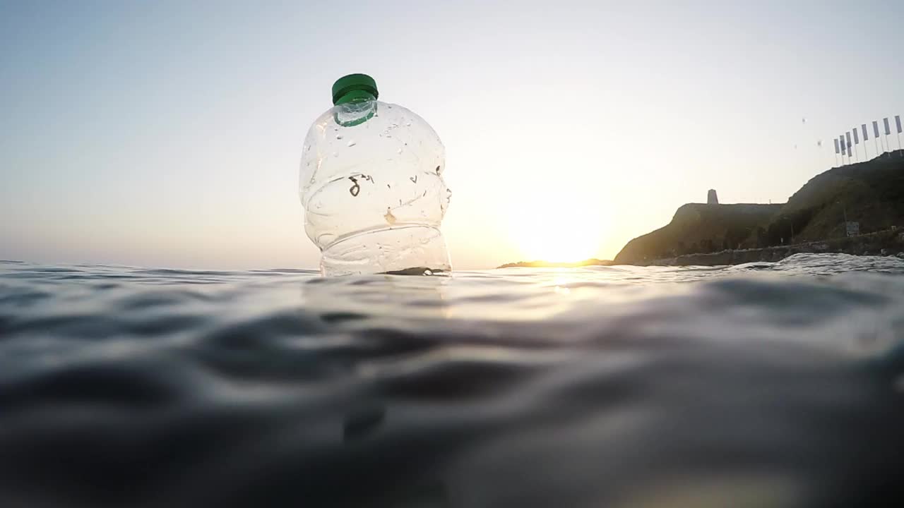 日落时分，塑料瓶里的泥土漂浮在海上。慢动作视频素材