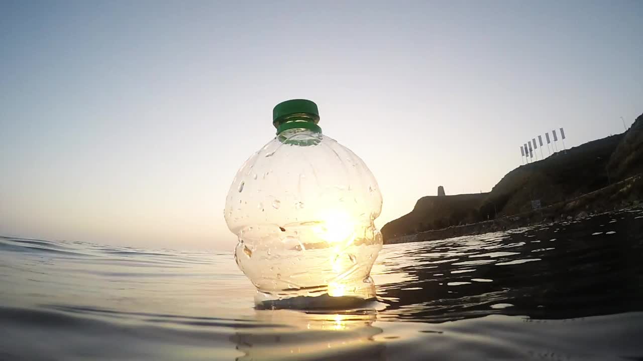 日落时分，塑料瓶漂浮在海上。慢动作视频素材