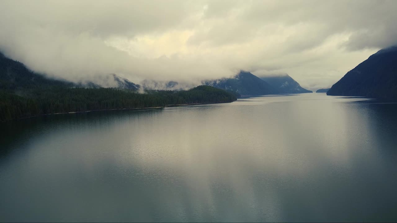 在有山脉和森林环绕的多云天气飞越湖面视频素材