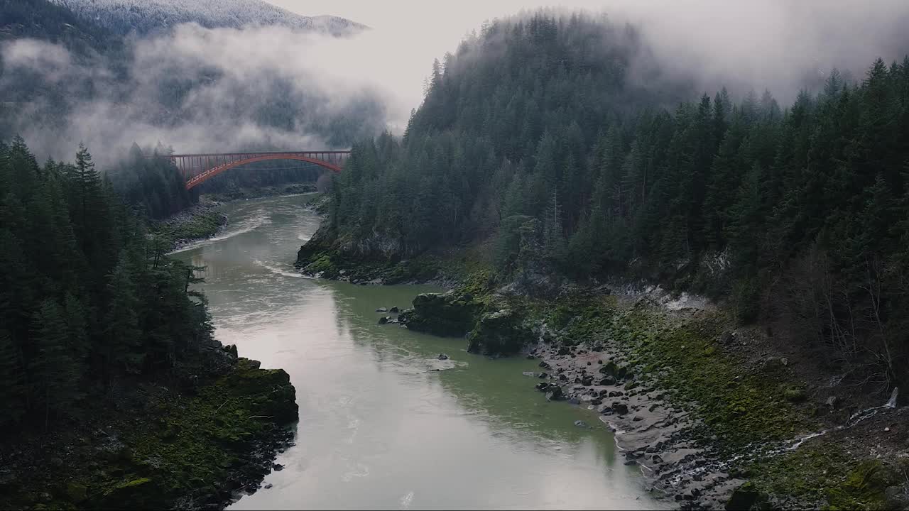 鸟瞰图的河流之间的山覆盖着森林。远处的云和旧桥视频素材