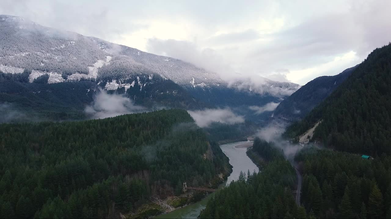 开镜头的河流在山谷环绕的绿色森林和雪山的山峰可见视频素材