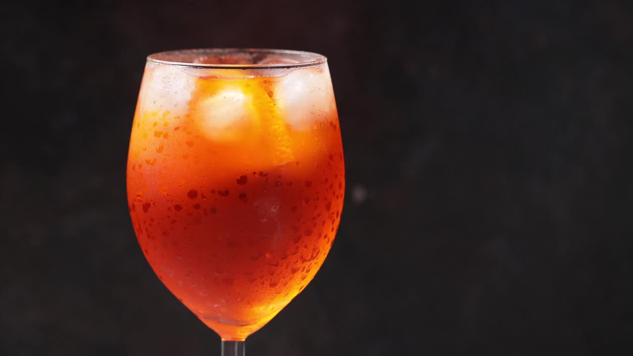 Aperol在黑色背景上喷鸡尾酒。勺子混合饮料。一杯夏日橙鸡尾酒。副本的空间。4 k视频素材