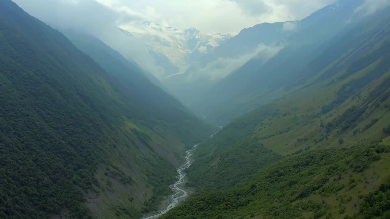 绿草如茵的小山和山间的河流。远处的雪峰视频素材