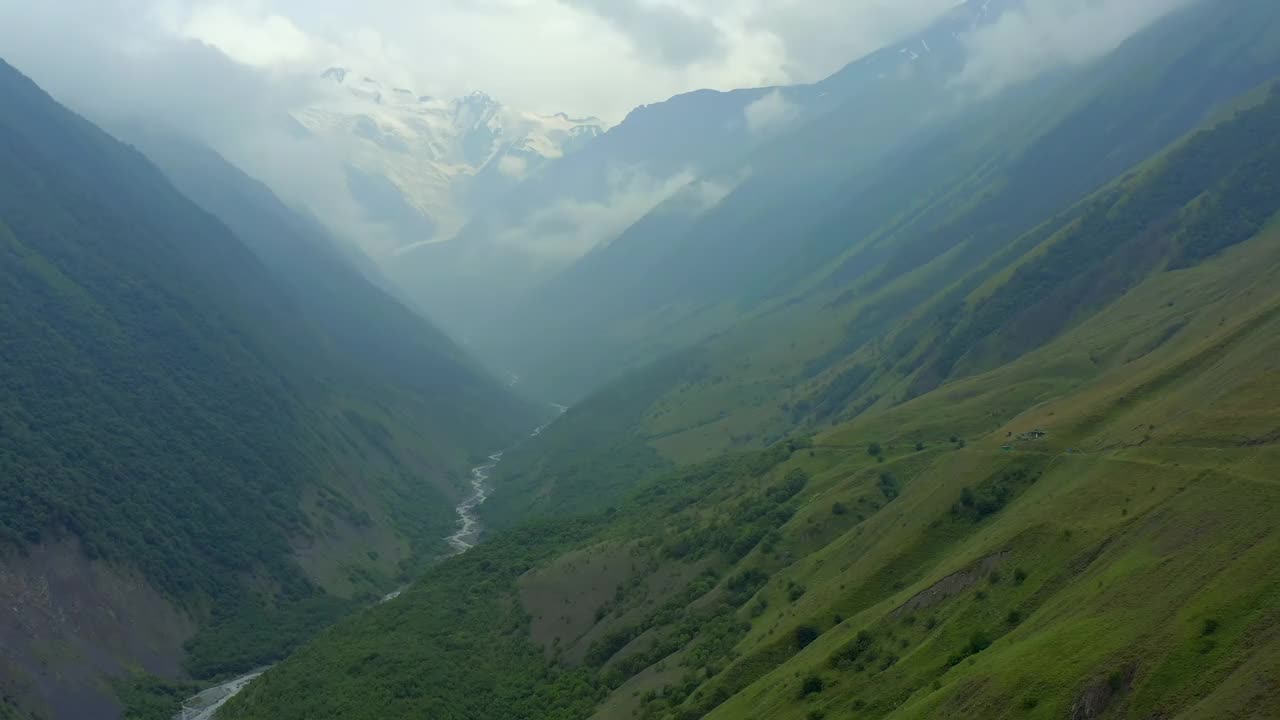 山谷中有绿色的小山和白雪皑皑的高山，距离很远。视频素材