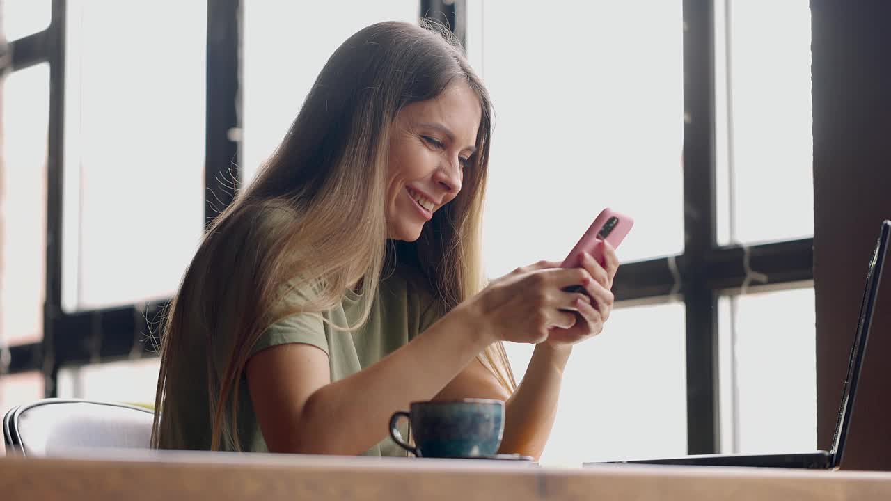 长发的年轻女子在咖啡馆边喝咖啡边聊手机视频素材