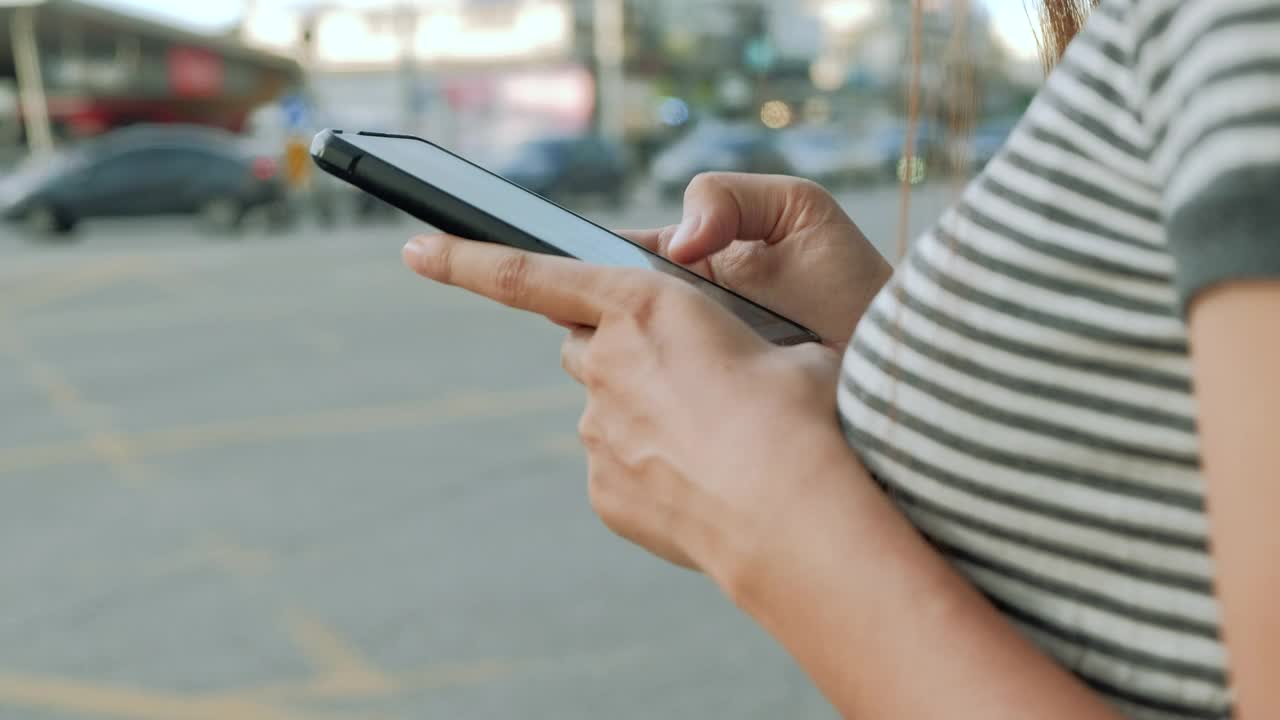 女人的手在城市购物街使用智能手机，搜索或社交网络的概念，关闭。视频素材