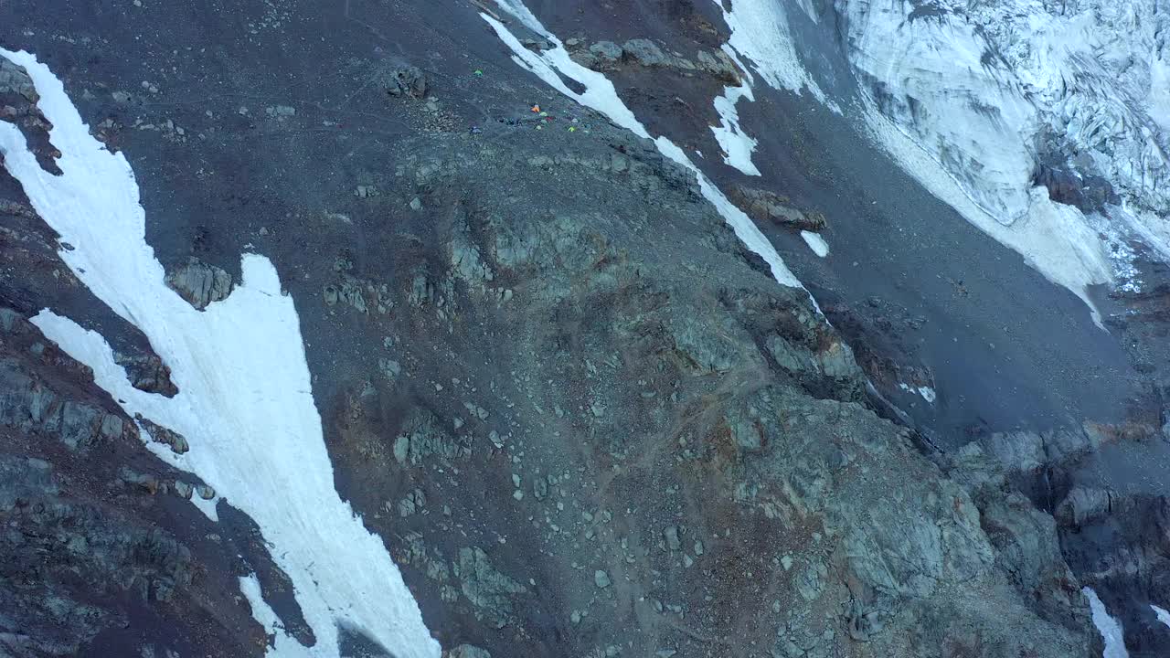 鸟瞰图:在冰川和积雪的岩石前，游客在高山上露营。视频素材