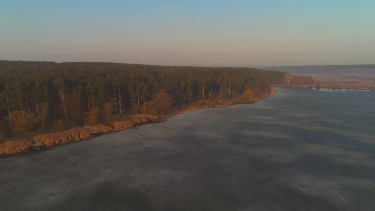 黄昏时绿色森林附近结冰的湖或池塘的空中景象视频素材