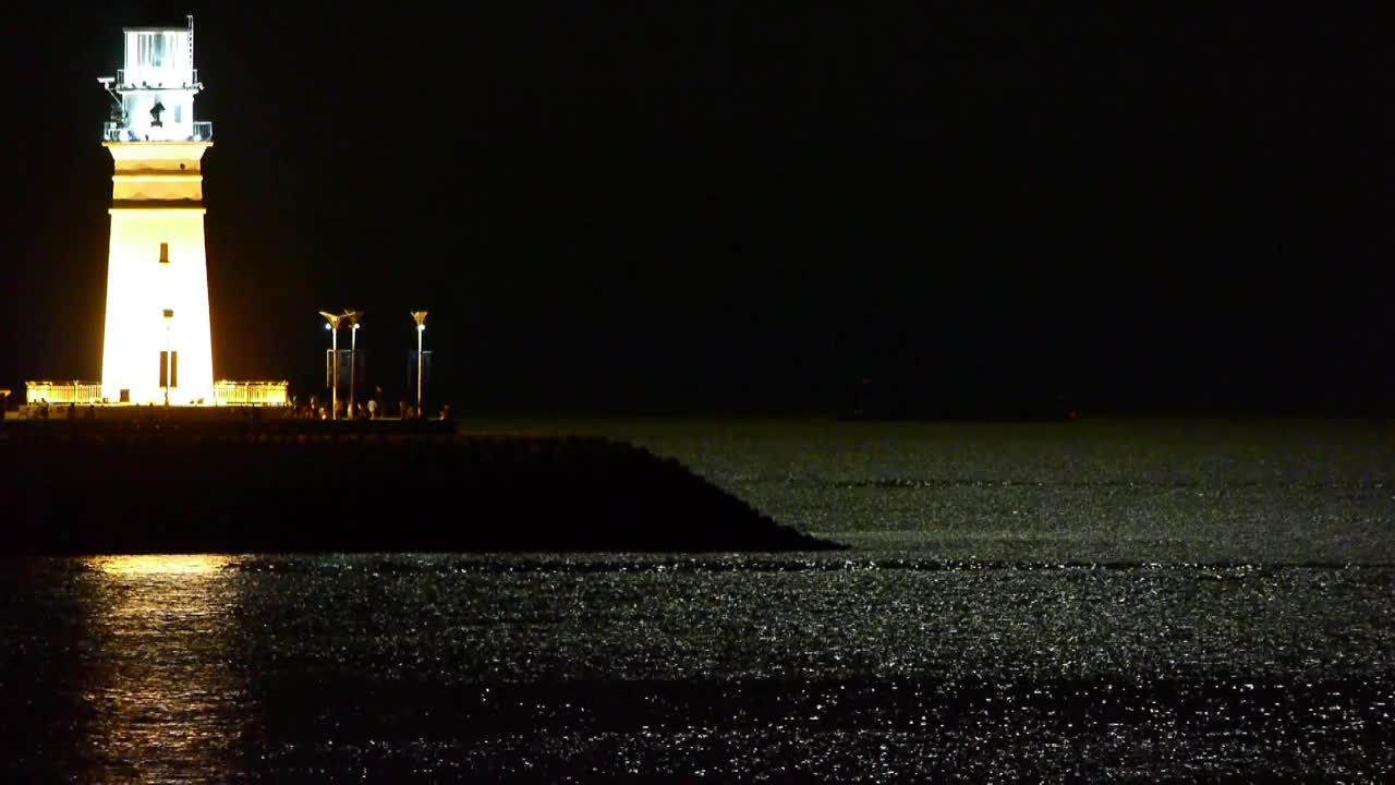 夜晚的灯塔，月光反射在海面上。视频素材