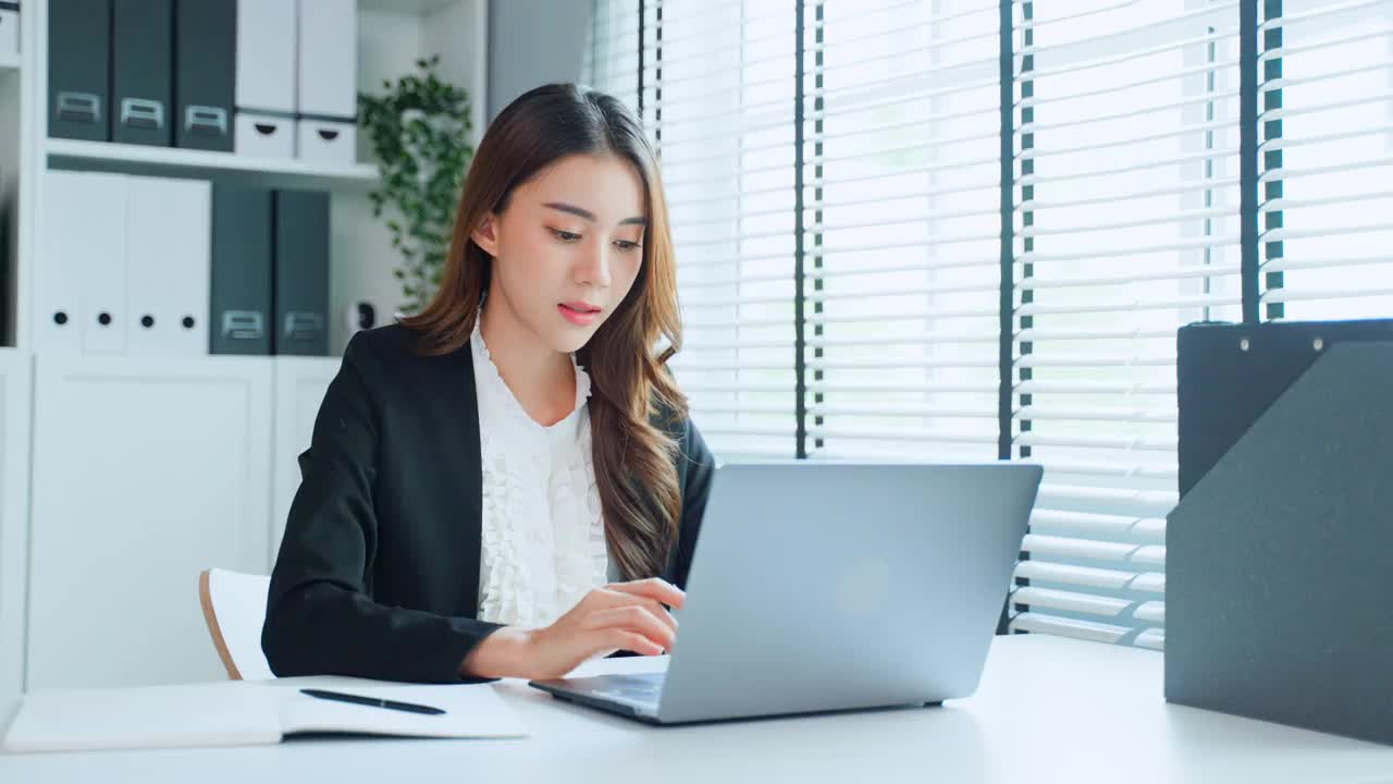 疲惫迷人的亚洲女商人在工作桌上看着许多文件工作。忙碌的女员工由于工作到很晚，在办公室的电脑桌上放着工作文件，感到疲惫头痛视频素材