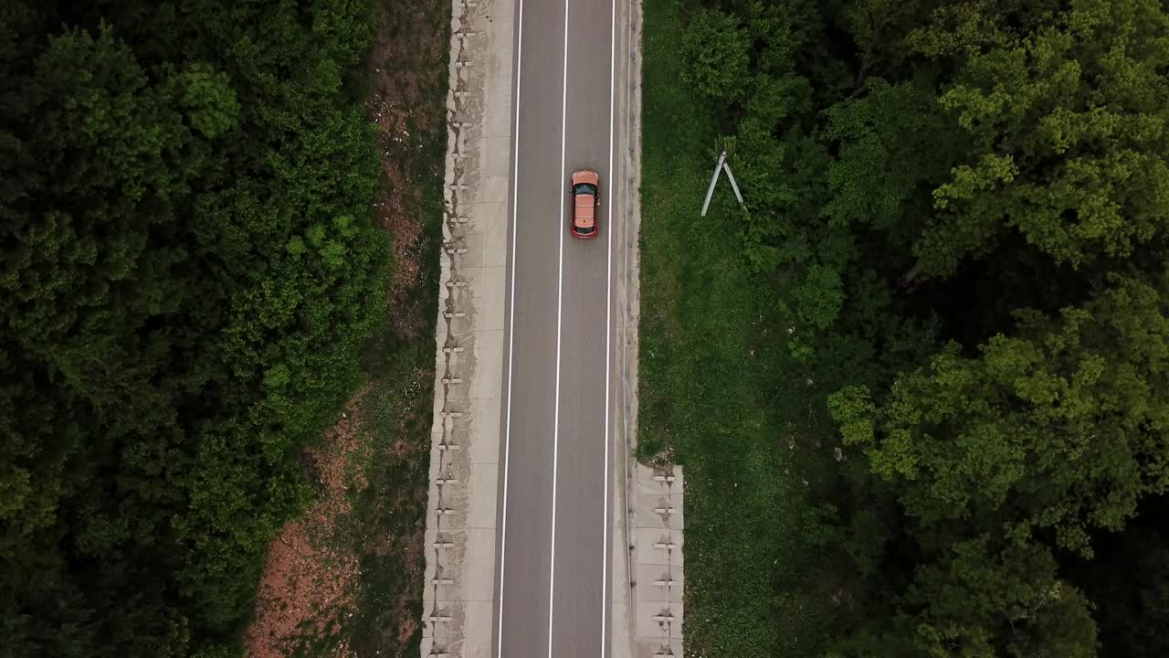 无人机视角，跟踪模式:鸟瞰图，在两车道乡村森林公路上空飞行，橙色的汽车移动，绿树茂密的森林生长在两侧。沿着森林道路行驶的汽车。视频素材