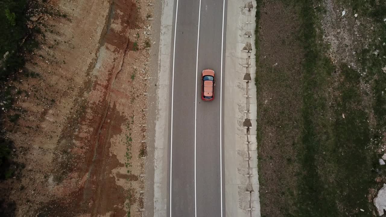 无人机视角，跟踪模式:鸟瞰图，在两车道乡村森林公路上空飞行，橙色的汽车移动，绿树茂密的森林生长在两侧。沿着森林道路行驶的汽车。视频素材