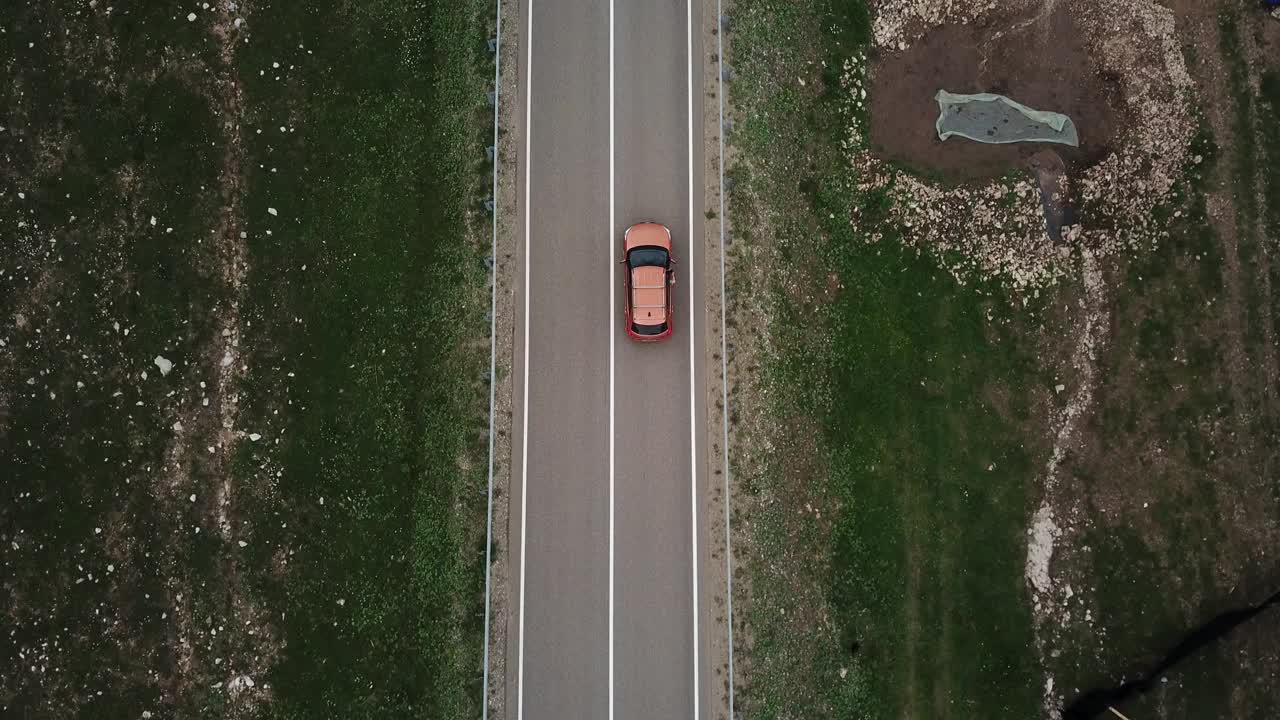 无人机视角，跟踪模式:鸟瞰图，在两车道乡村森林公路上空飞行，橙色的汽车移动，绿树茂密的森林生长在两侧。沿着森林道路行驶的汽车。视频素材