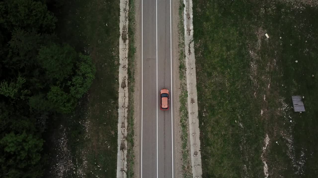 无人机视角，跟踪模式:鸟瞰图，在两车道乡村森林公路上空飞行，橙色的汽车移动，绿树茂密的森林生长在两侧。沿着森林道路行驶的汽车。视频素材