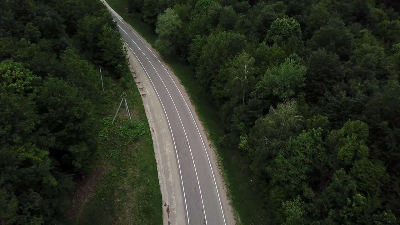 无人机视角，跟踪模式:鸟瞰图，在两车道乡村森林公路上空飞行，橙色的汽车移动，绿树茂密的森林生长在两侧。沿着森林道路行驶的汽车。视频素材