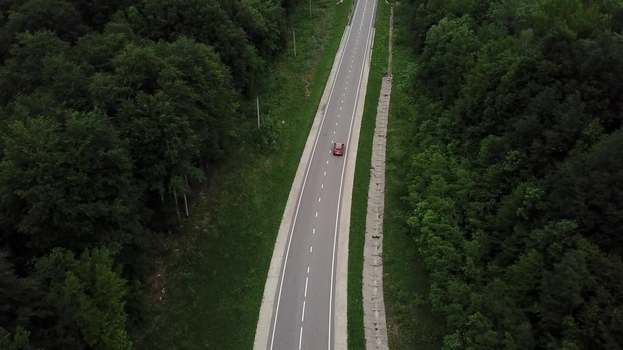 无人机视角，跟踪模式:鸟瞰图，在两车道乡村森林公路上空飞行，橙色的汽车移动，绿树茂密的森林生长在两侧。沿着森林道路行驶的汽车。视频素材