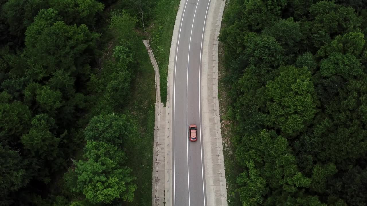 无人机视角，跟踪模式:鸟瞰图，在两车道乡村森林公路上空飞行，橙色的汽车移动，绿树茂密的森林生长在两侧。沿着森林道路行驶的汽车。视频素材