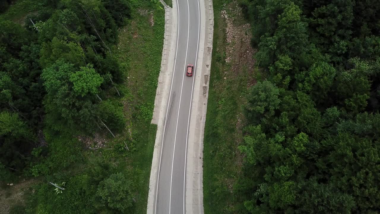 无人机视角，跟踪模式:鸟瞰图，在两车道乡村森林公路上空飞行，橙色的汽车移动，绿树茂密的森林生长在两侧。沿着森林道路行驶的汽车。视频素材