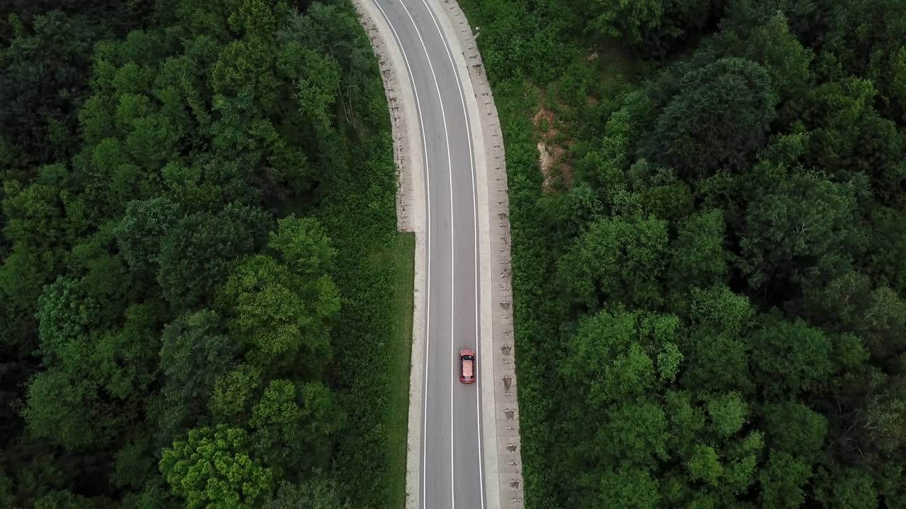 无人机视角，跟踪模式:鸟瞰图，在两车道乡村森林公路上空飞行，橙色的汽车移动，绿树茂密的森林生长在两侧。沿着森林道路行驶的汽车。视频素材