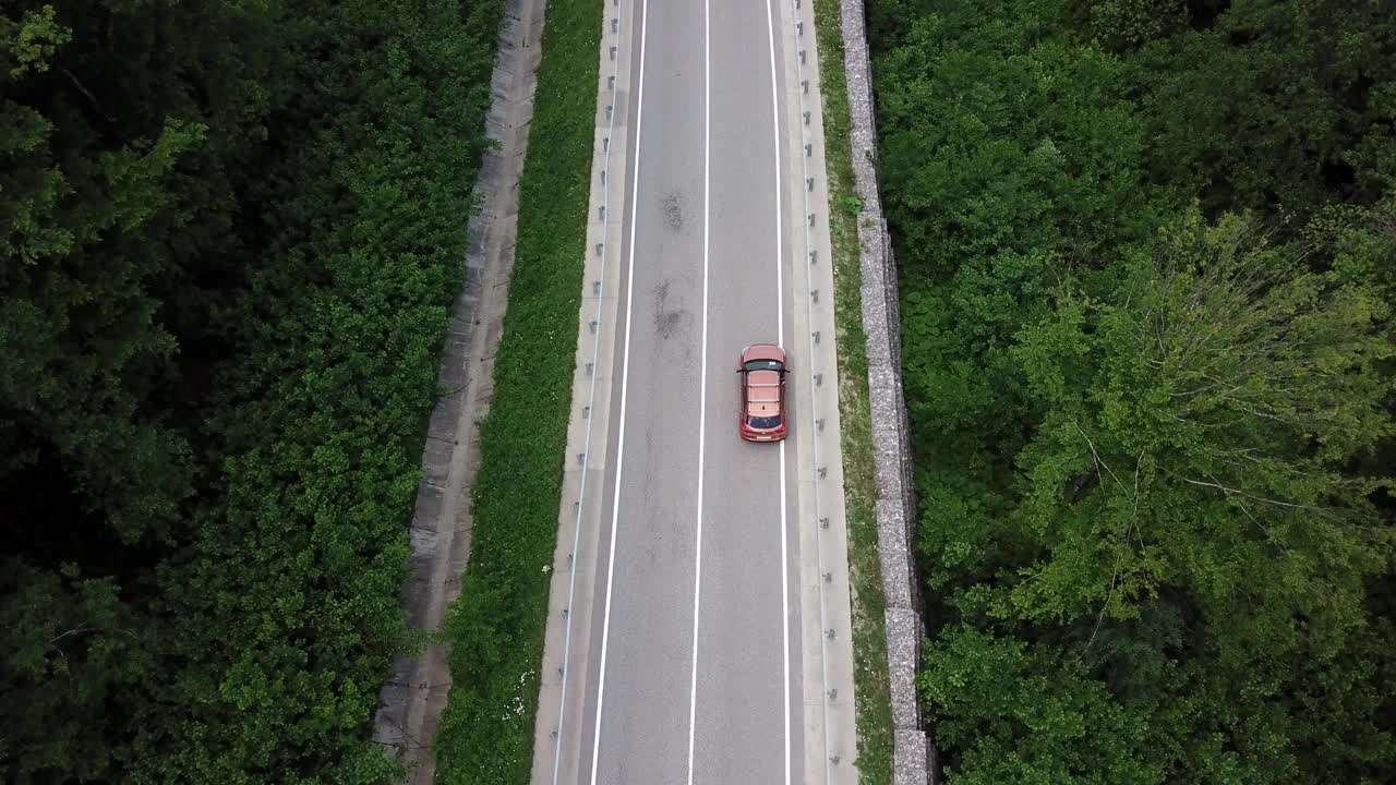 无人机视角，跟踪模式:鸟瞰图，在两车道乡村森林公路上空飞行，橙色的汽车移动，绿树茂密的森林生长在两侧。沿着森林道路行驶的汽车。视频素材