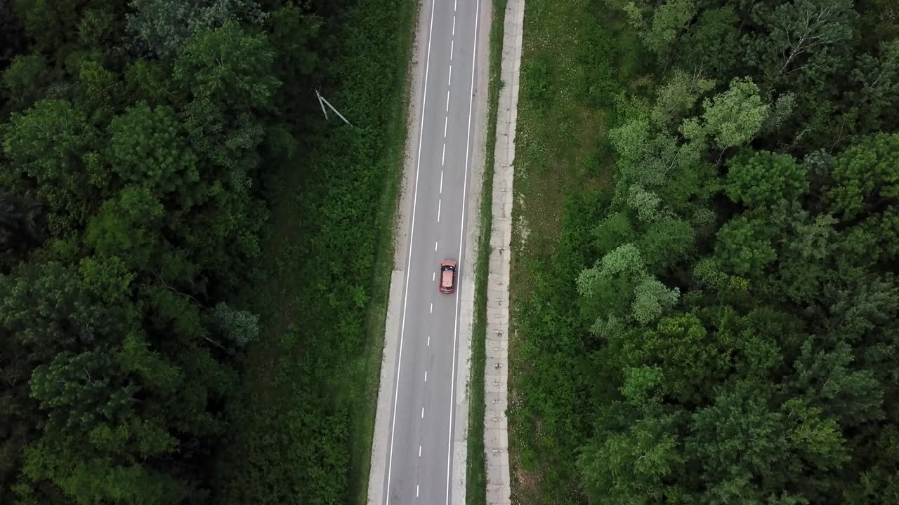 无人机视角，跟踪模式:鸟瞰图，在两车道乡村森林公路上空飞行，橙色的汽车移动，绿树茂密的森林生长在两侧。沿着森林道路行驶的汽车。视频素材