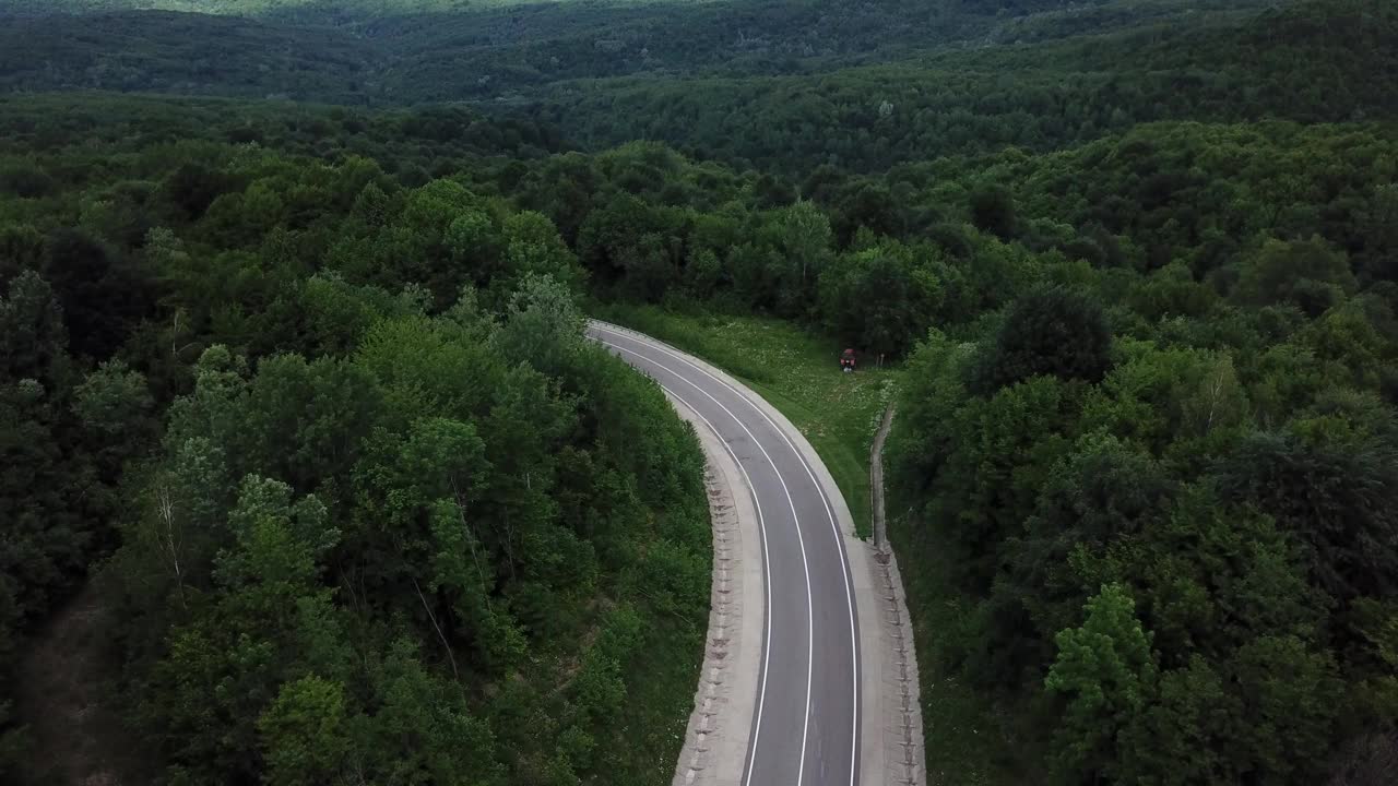 无人机视角，跟踪模式:鸟瞰图，在两车道乡村森林公路上空飞行，橙色的汽车移动，绿树茂密的森林生长在两侧。沿着森林道路行驶的汽车。视频素材