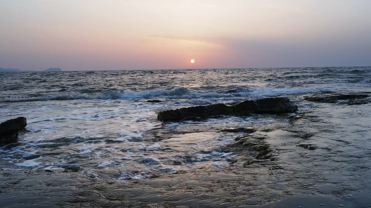 日出时的海岸线景观，太阳在地平线上，海浪拍打着海岸。视频素材