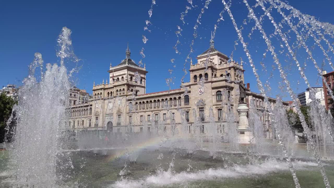 西班牙，巴利亚多利德广场(José Zorrilla of Valladolid)上的喷泉的管道形成了彩虹，背景是西班牙的骑兵学院视频素材