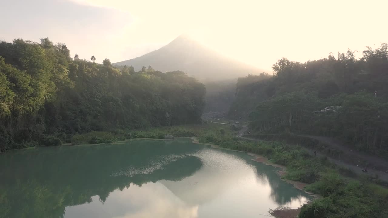 无人机拍摄的湖泊和火山在日出时爆发的自然景观。湖被树木环绕着。你还可以看到从火山喷发出来的物质经过的河流视频素材