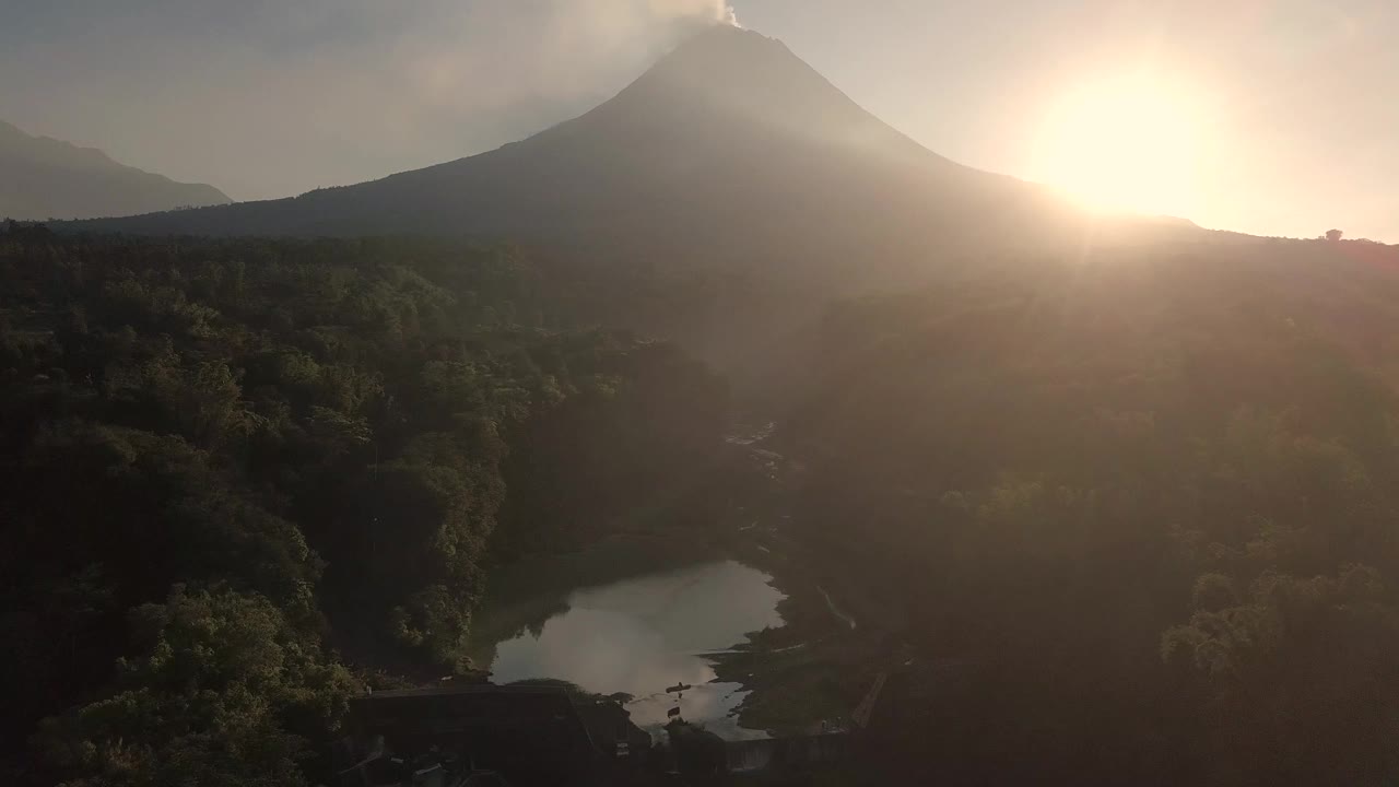 无人机拍摄的湖泊和火山在日出时爆发的自然景观。湖被树木环绕着。你还可以看到从火山喷发出来的物质经过的河流视频素材