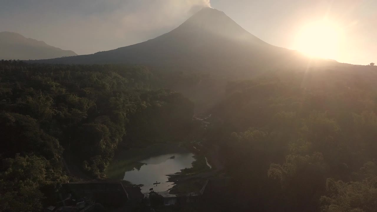 无人机拍摄的湖泊和火山在日出时爆发的自然景观。湖被树木环绕着。你还可以看到从火山喷发出来的物质经过的河流视频素材