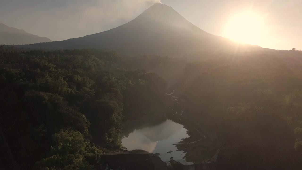 无人机拍摄的湖泊和火山在日出时爆发的自然景观。湖被树木环绕着。你还可以看到从火山喷发出来的物质经过的河流视频素材