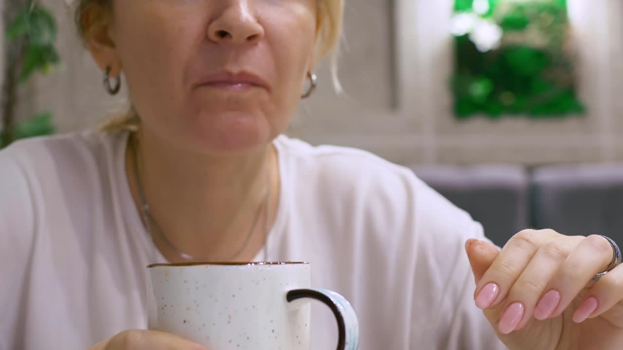 特写的一个女人正在咖啡馆里吃早餐，桌上有一杯咖啡。这个女人的指甲修剪得很好，还涂了粉红色的指甲油视频素材