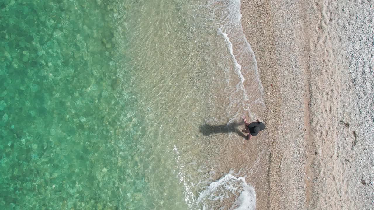 女人走在田园诗般的海滩上，海浪在慢动作中飞溅，鸟瞰图视频素材