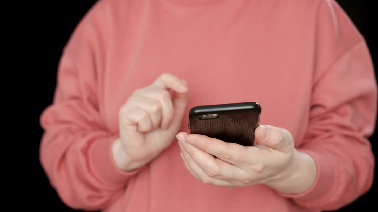 特写女性在黑色背景下使用手机、触摸屏或短信的双手。拿着智能手机浏览社交网络的女人。视频素材