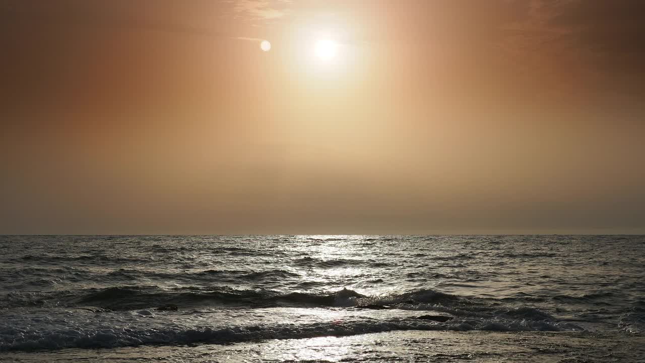 日出时的海岸线景观，太阳在地平线上，海浪拍打着海岸。视频素材