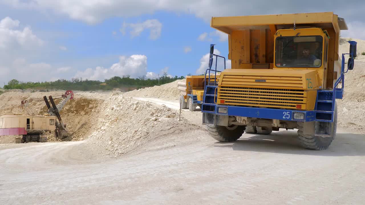 在建筑工地上工作的挖掘机。一台挖掘机和一辆卡车在挖掘和装载建筑土。一个工业区。开放地区的工业。工业水泥加工设备。视频素材