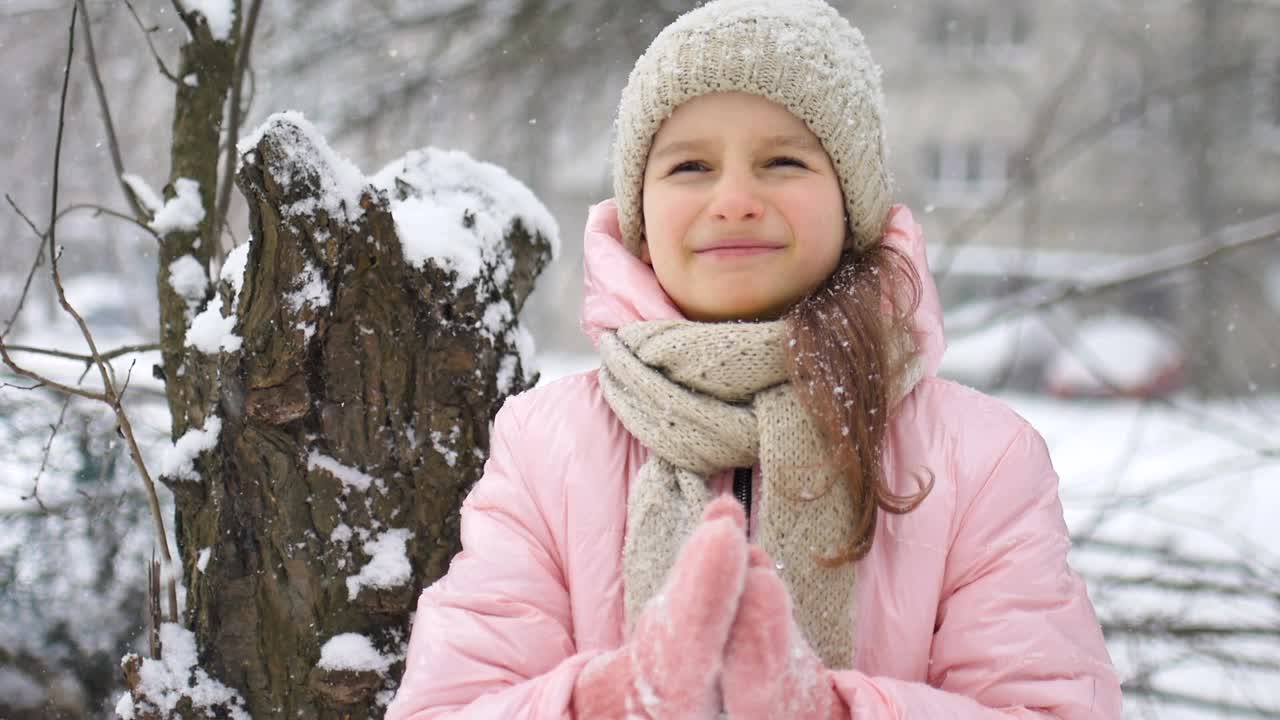 一个女孩在冬天玩雪，穿着冬衣在户外闭着眼睛用舌头吃雪。快乐的童年和积极的假期概念视频素材