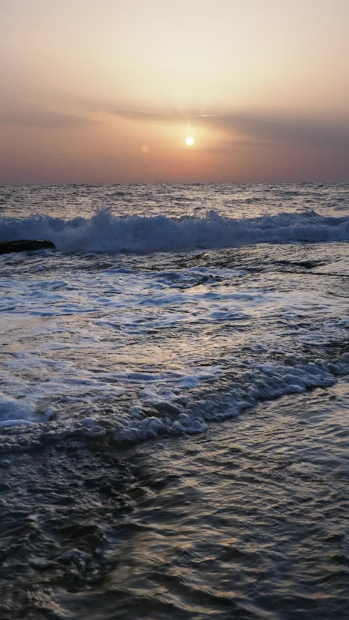 日出时的海岸线景观，太阳在地平线上，海浪拍打着海岸。视频素材