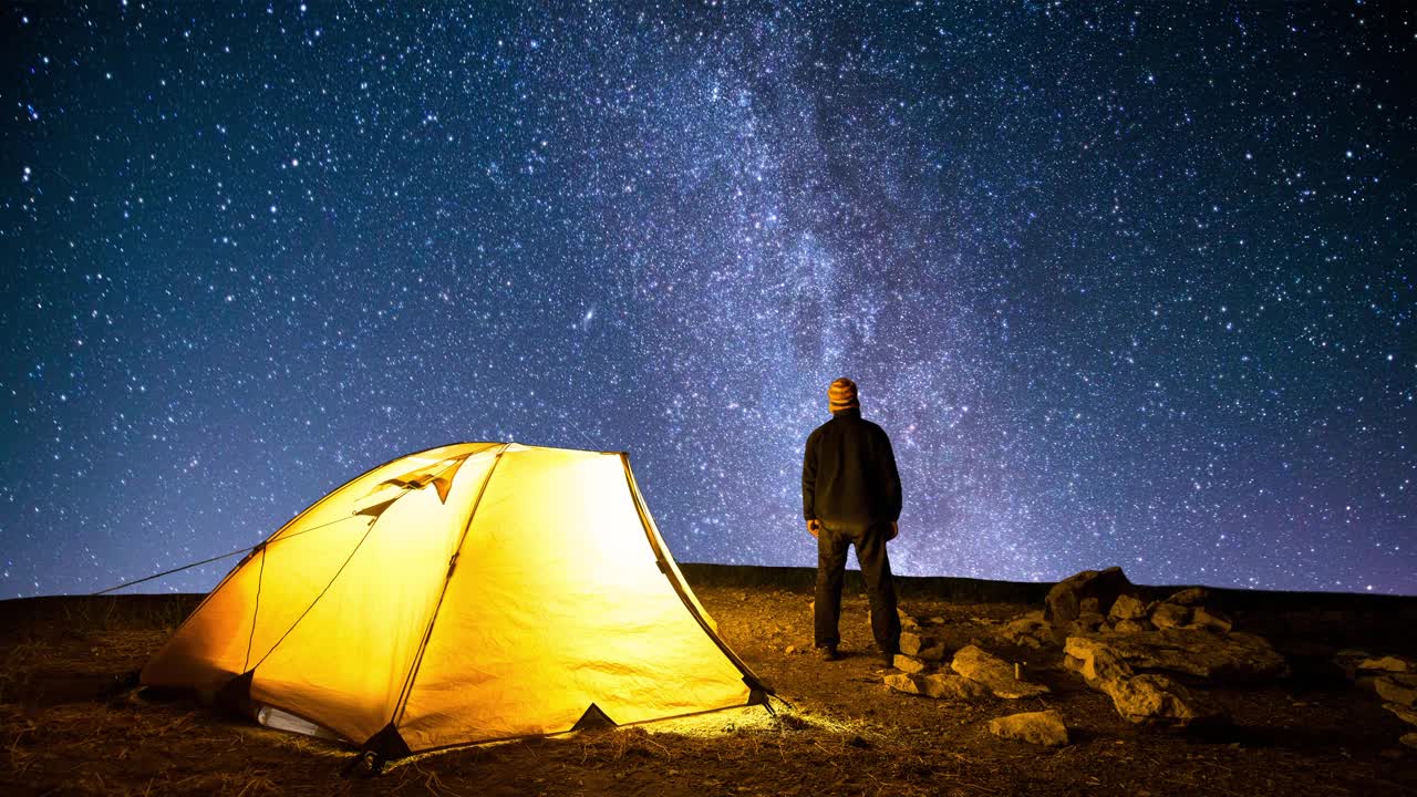 旅行者在闪烁的星空背景下，靠近发光的露营帐篷。Cinemagraph。视频素材