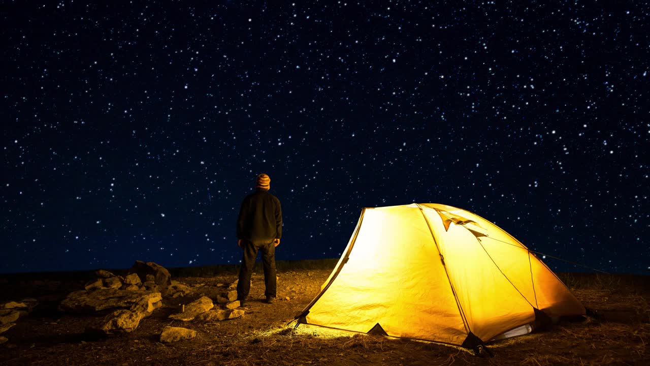 旅行者在闪烁的星空背景下，靠近发光的露营帐篷。Cinemagraph。视频素材