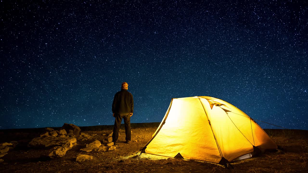 旅行者靠近发光的露营帐篷的背景上的星星在夜空中圈。Cinemagraph和延时。视频素材