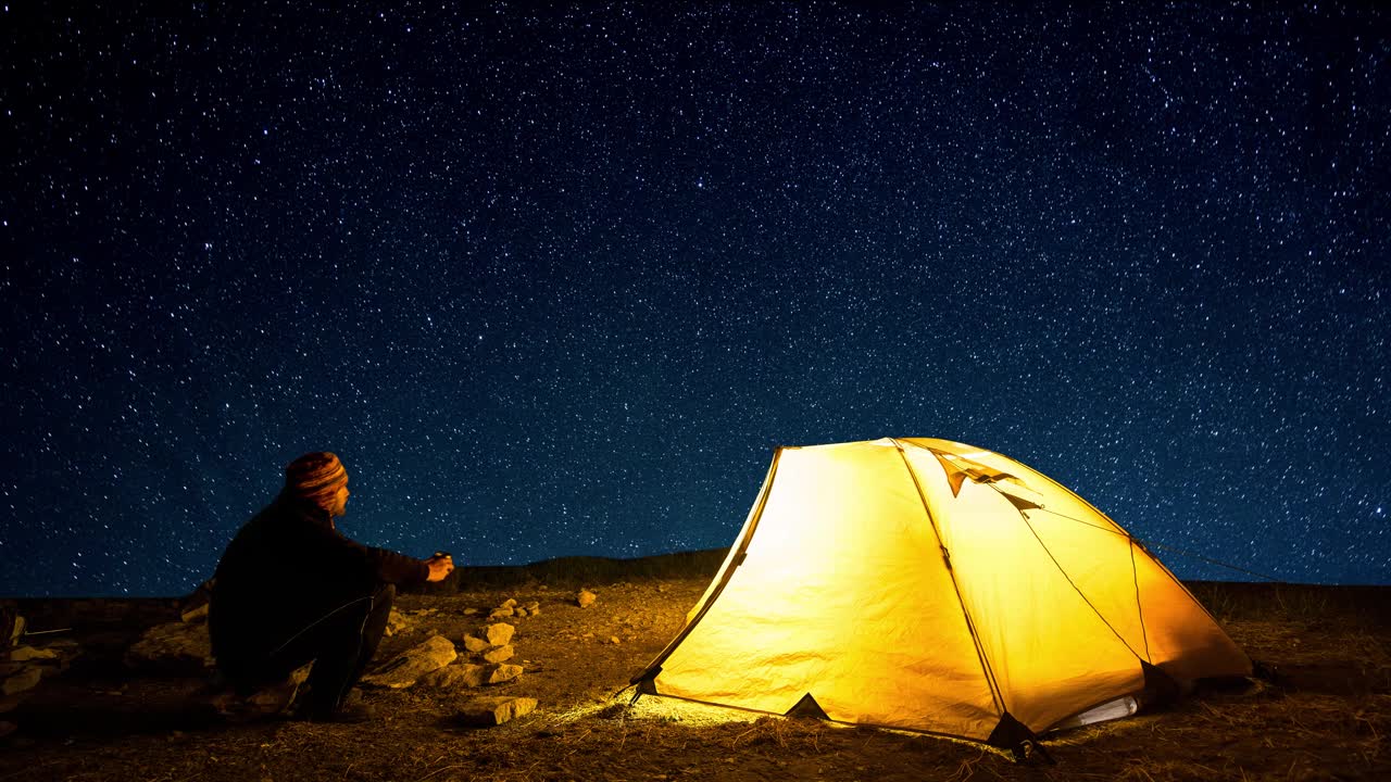 旅行者靠近发光的露营帐篷的背景上的星星在夜空中圈。Cinemagraph和延时。视频素材