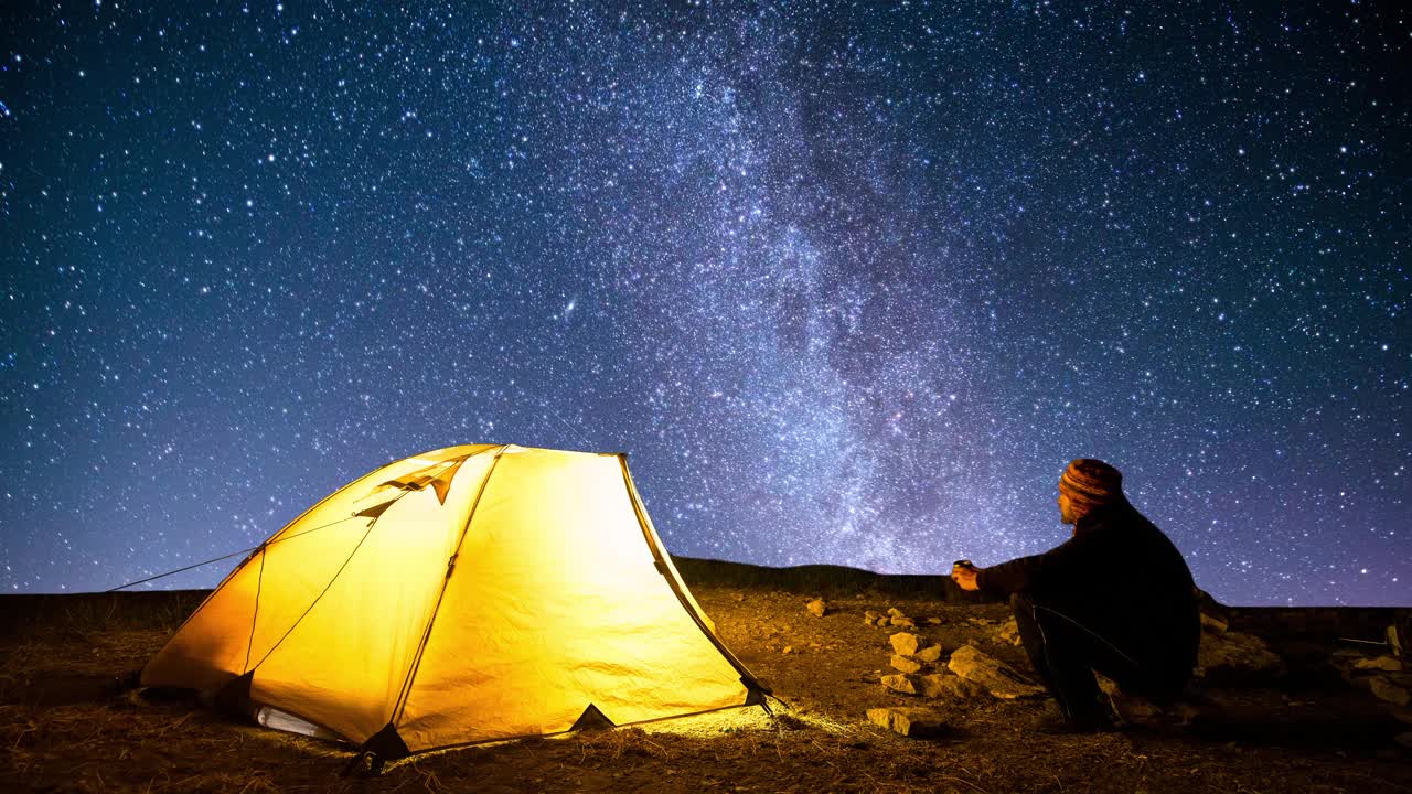 旅行者在闪烁的星空背景下，靠近发光的露营帐篷。Cinemagraph。视频素材