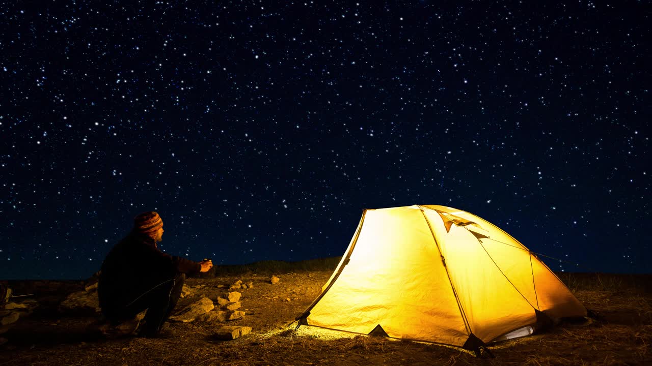 旅行者在闪烁的星空背景下，靠近发光的露营帐篷。Cinemagraph。视频素材